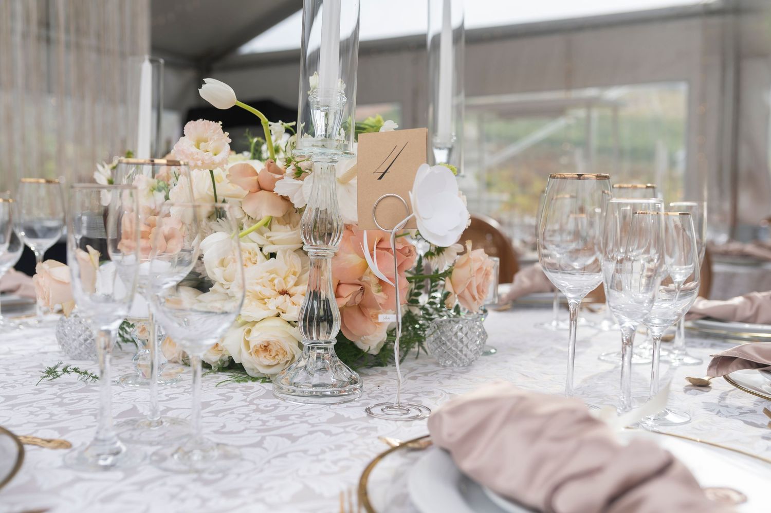 Elegant table settings with tall glass centerpieces and blush pink floral arrangements at a wedding reception.