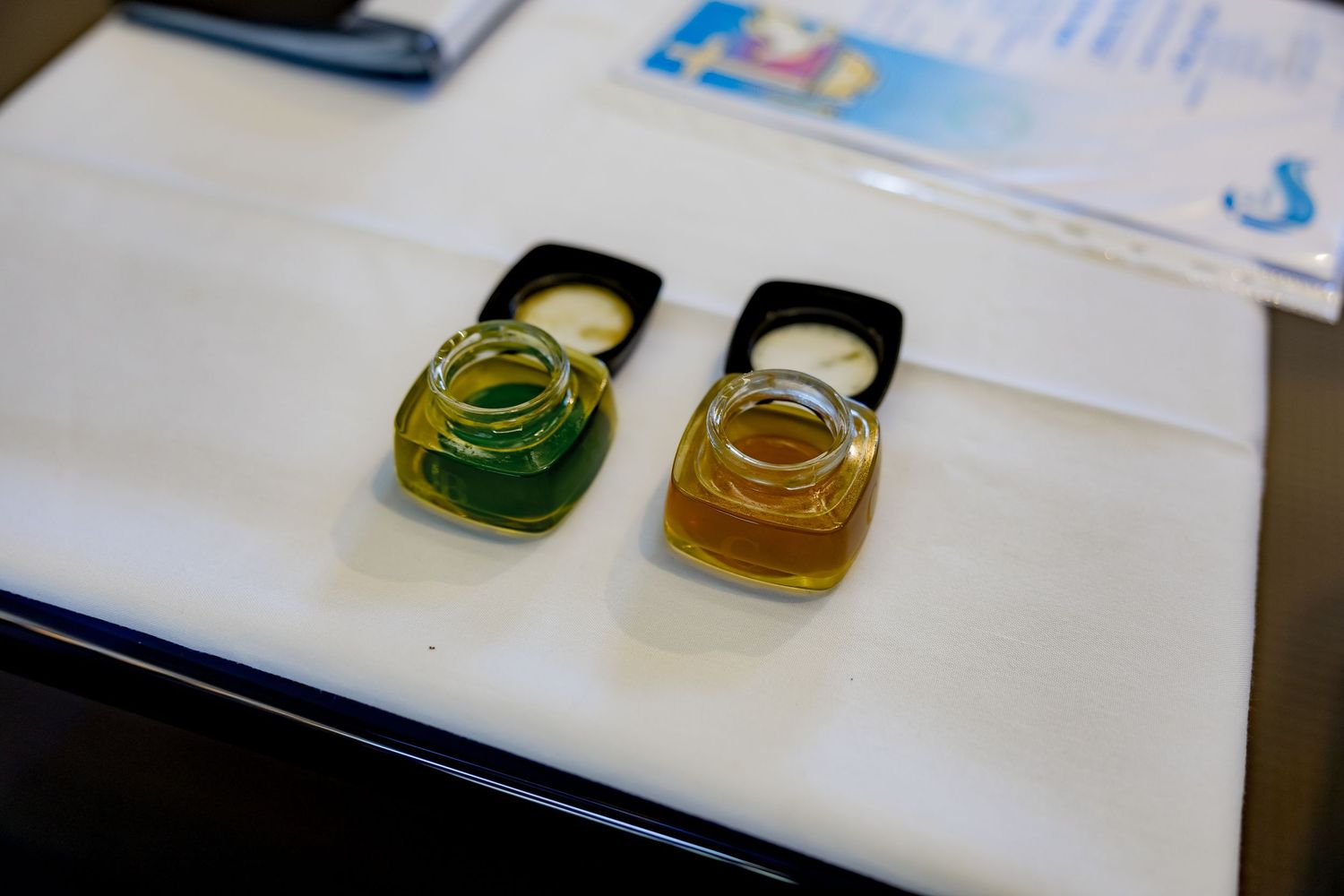 Close-up view of amber and green colored liquids in small glass vials on a white laboratory surface.