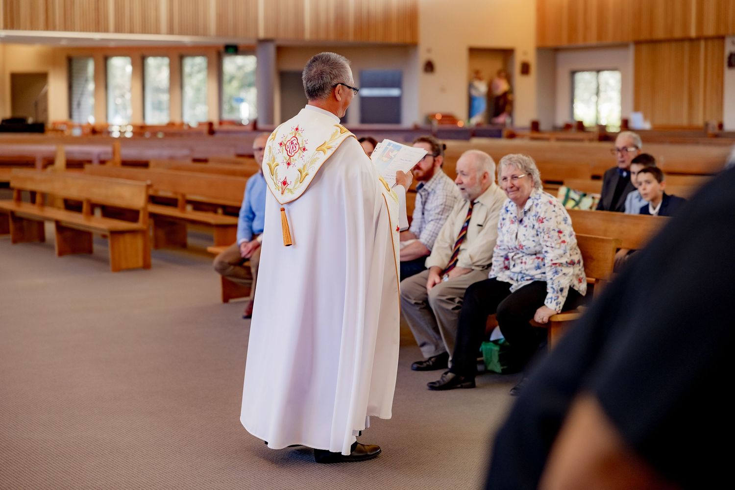 People sitting in wooden pews at a church gathering with warm lighting and wooden paneled walls.