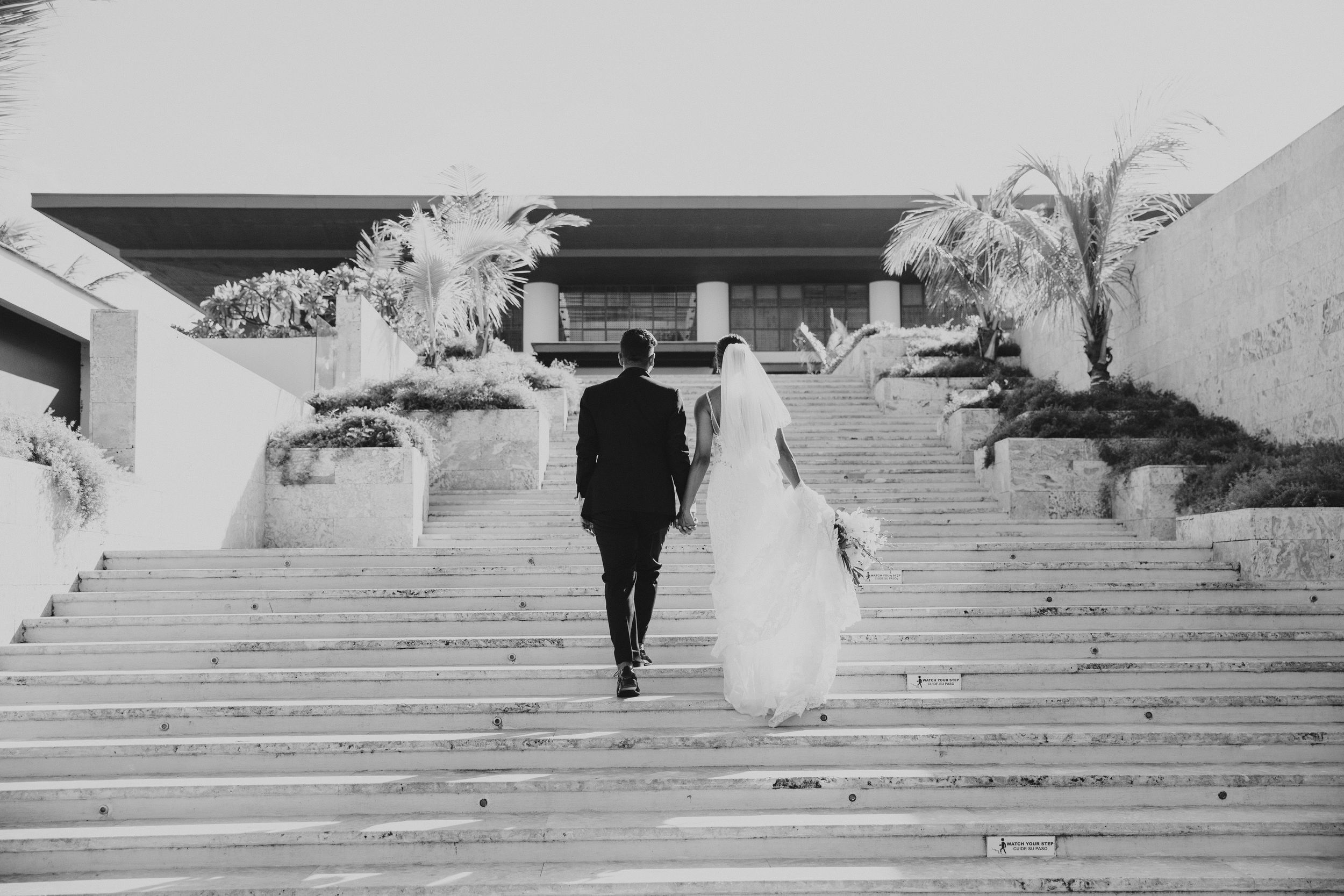 Black and white photo of wedding couple ascending grand outdoor stone staircase.