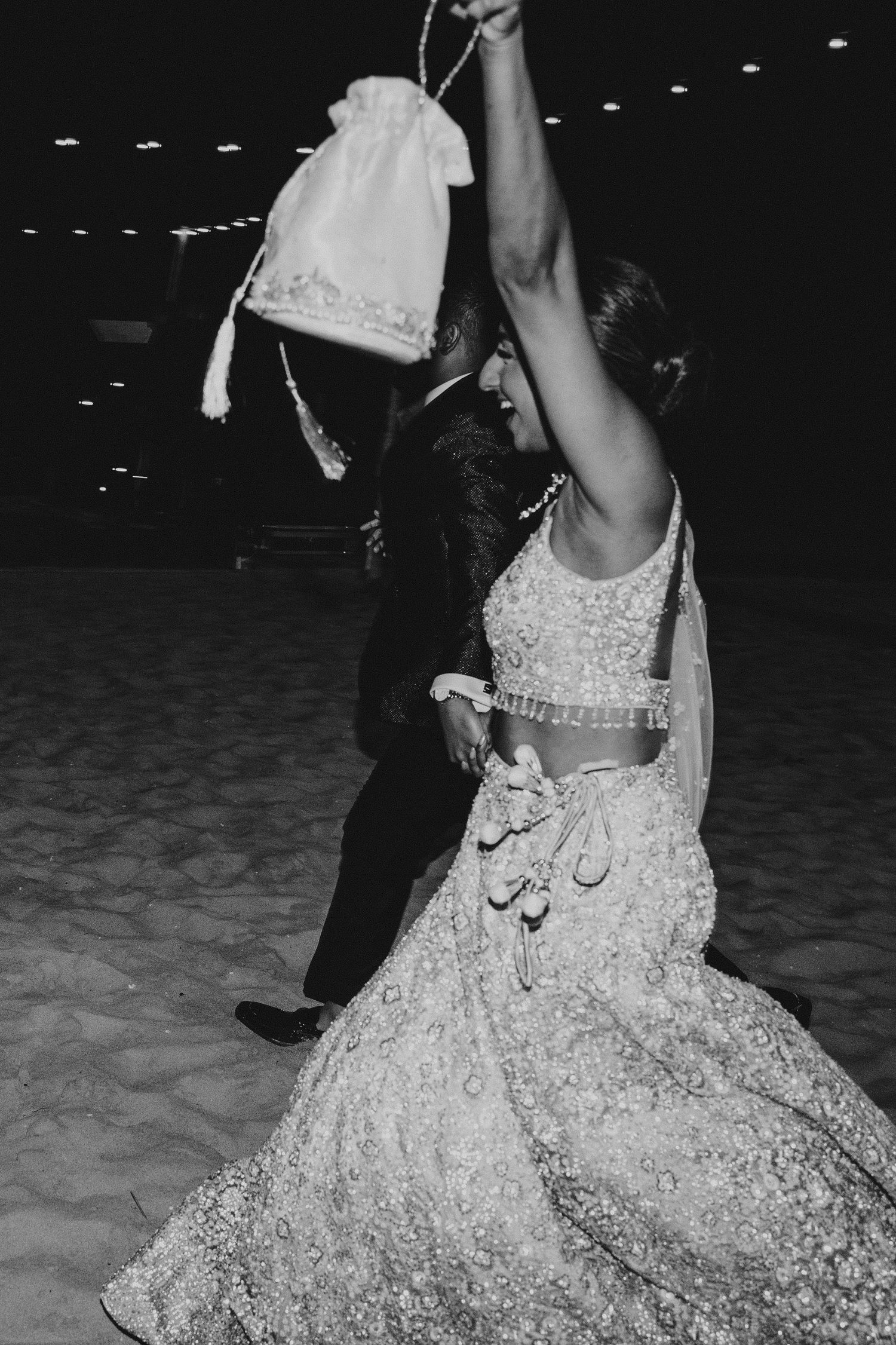 Person wearing an ornate white wedding dress dancing on a beach at night.