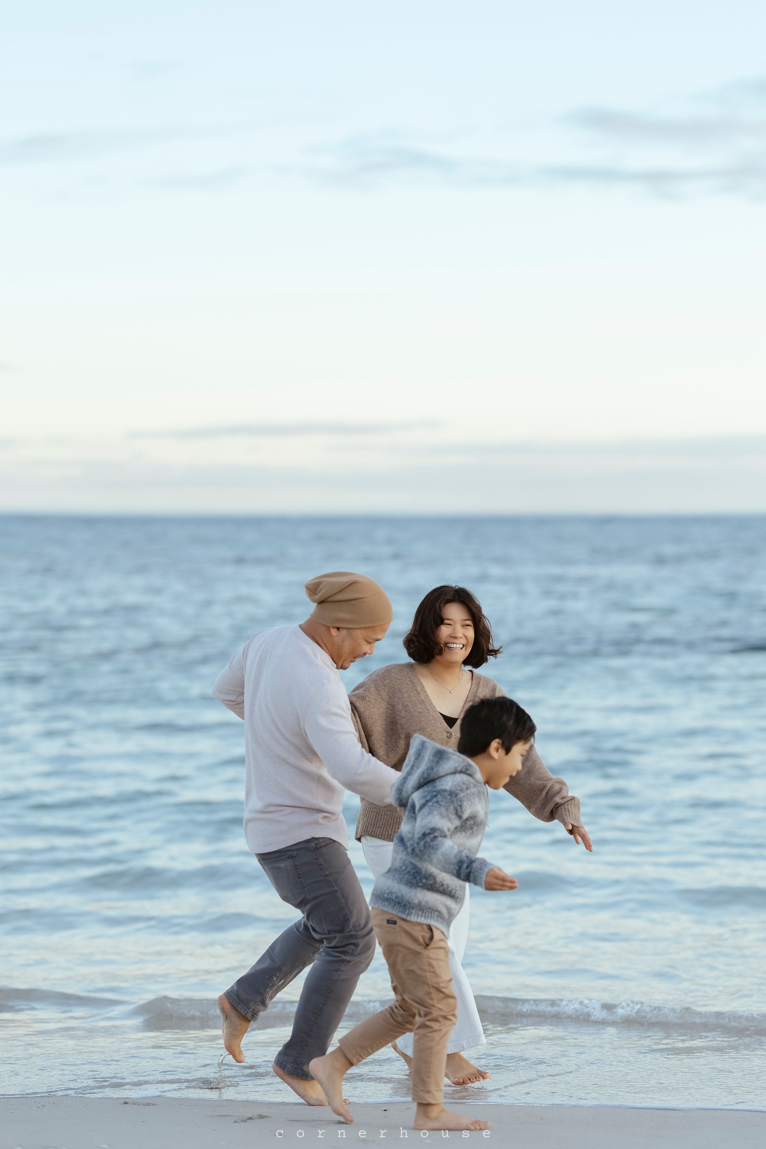 Family enjoys playful moment running and splashing together along beach shoreline at sunset.