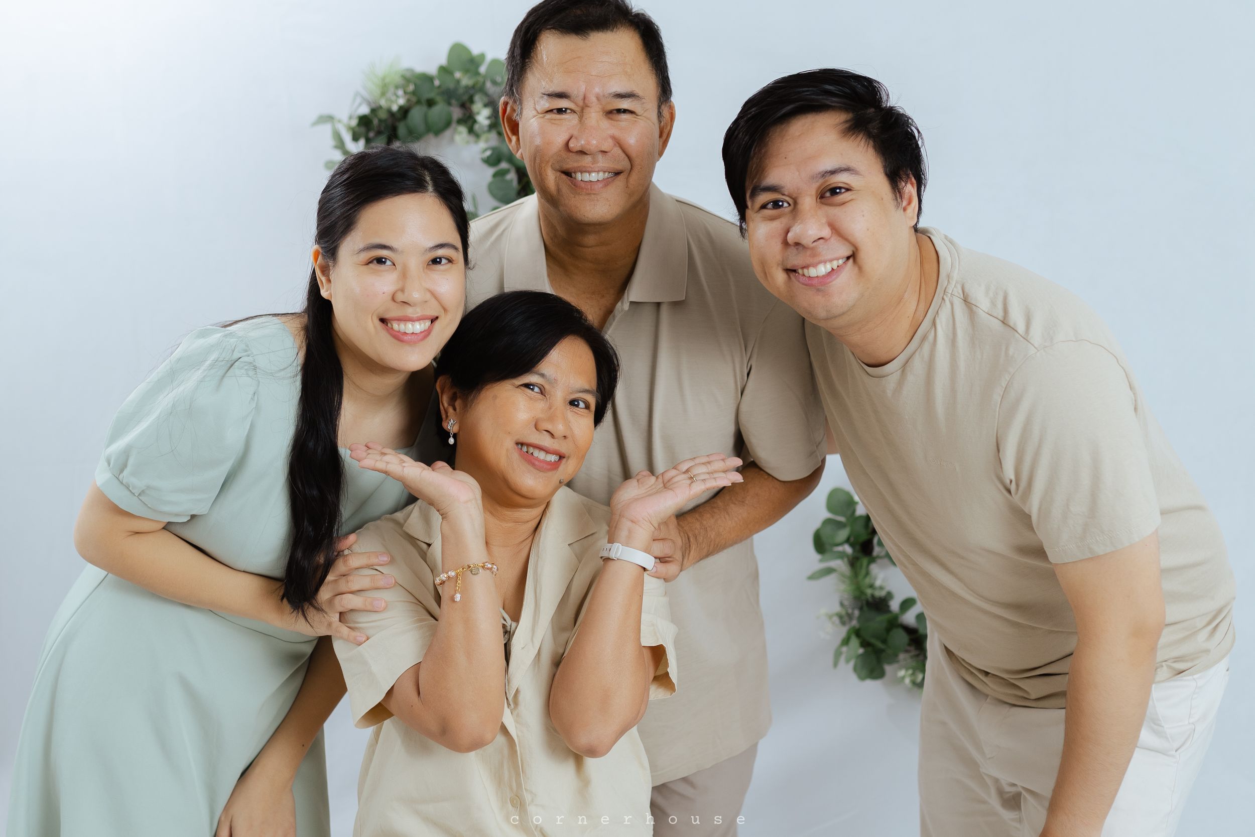 A family of four wearing casual attire poses together against a white background, smiling warmly at the camera.