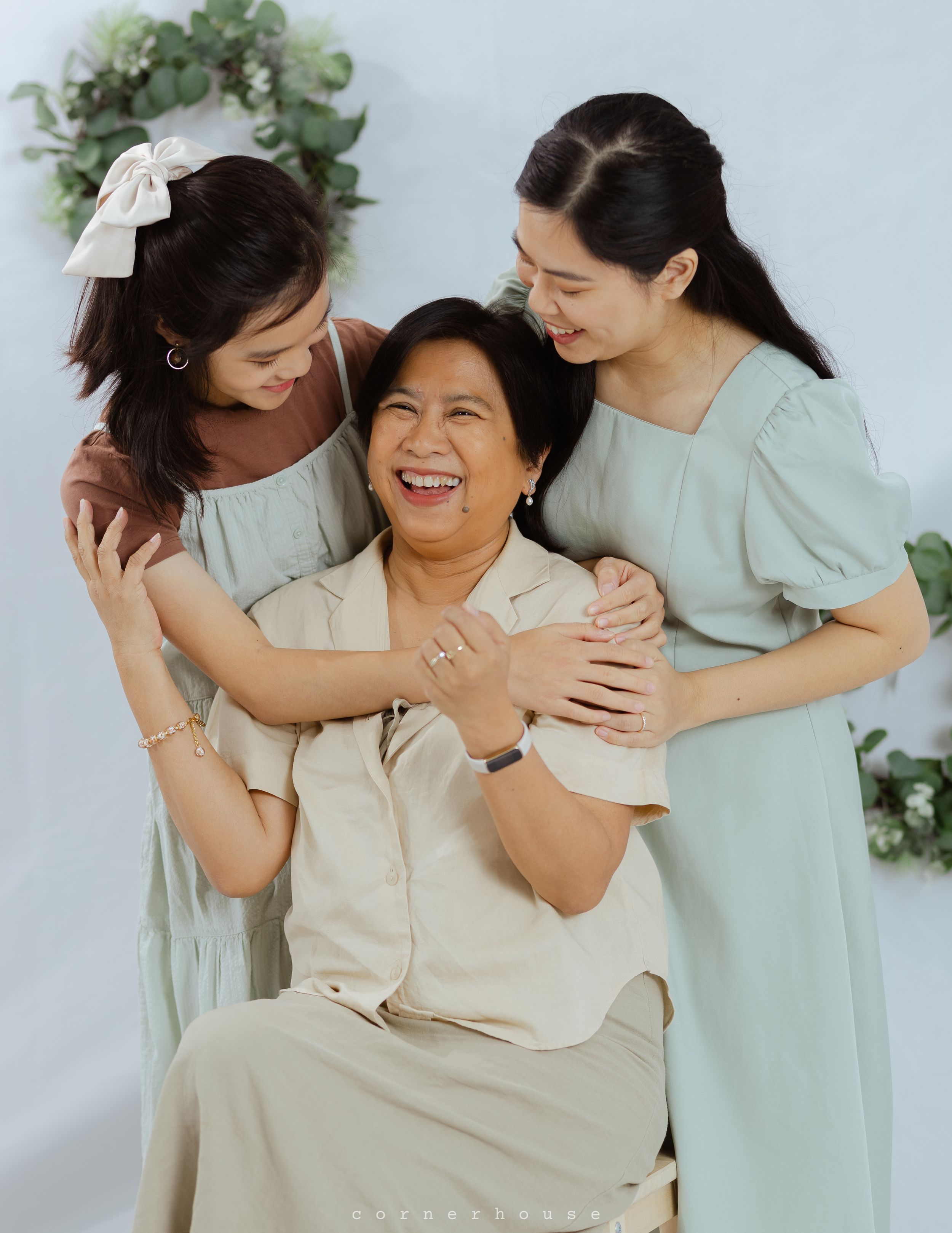 Three people sharing an intimate moment of joy and laughter while embracing against a light background with greenery.