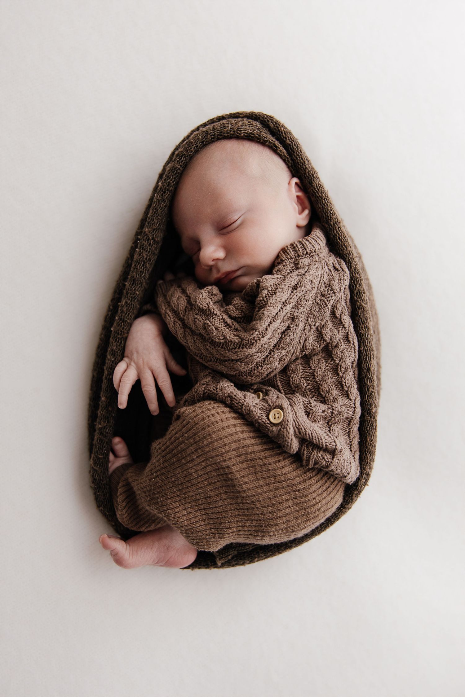 A sleeping newborn baby swaddled in cream-colored fabric lies peacefully in multiple similar poses.