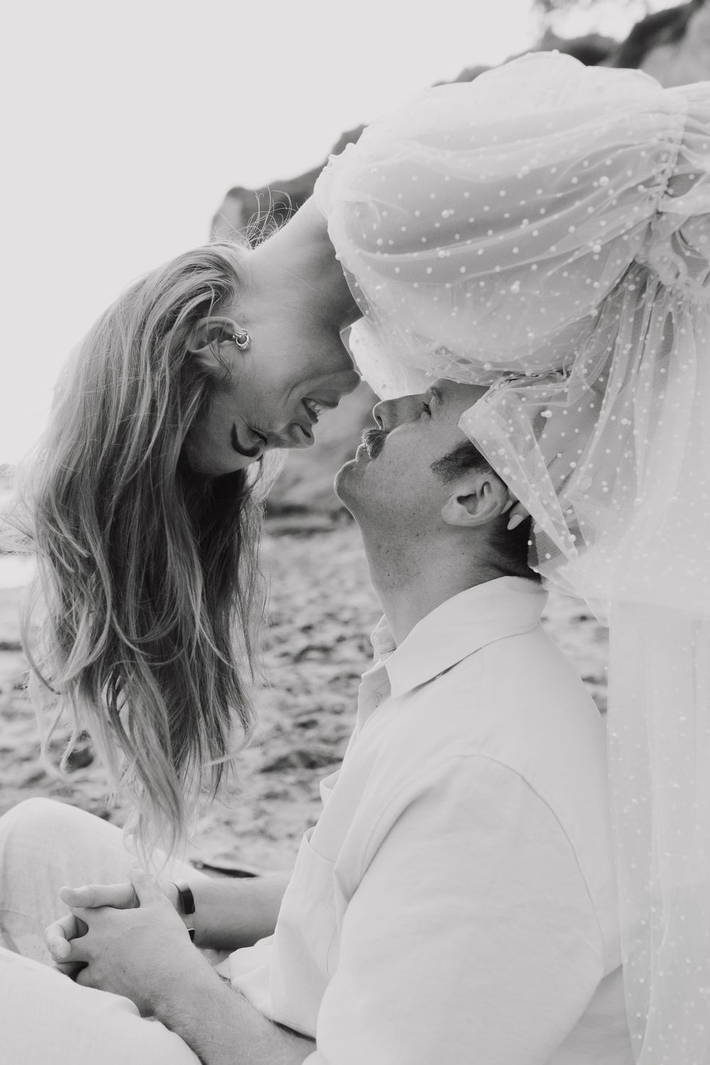 Intimate black and white beach portrait through delicate veil fabric.