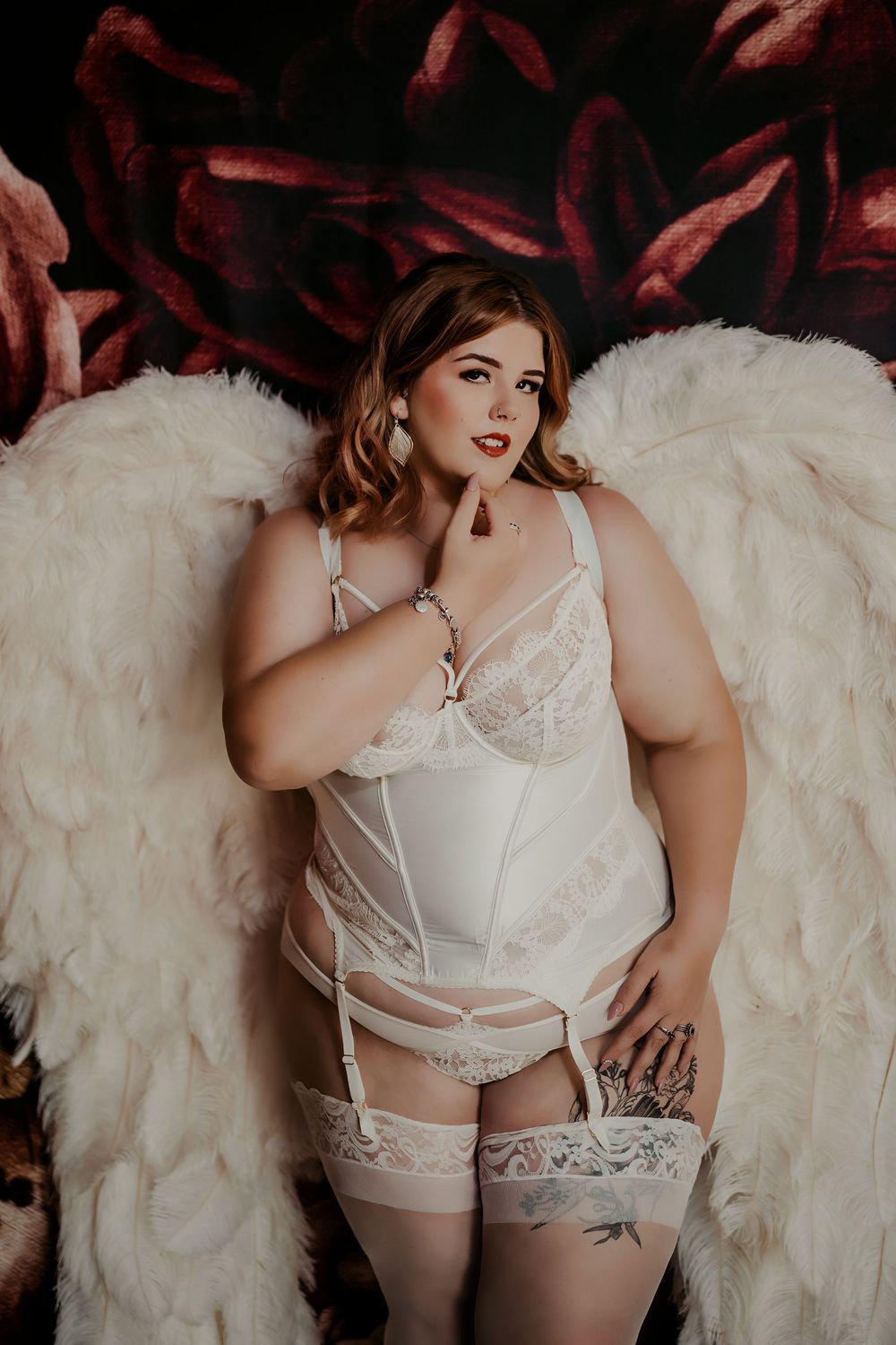 A vintage-inspired boudoir photo featuring white angel wings and delicate lingerie against a dark background.