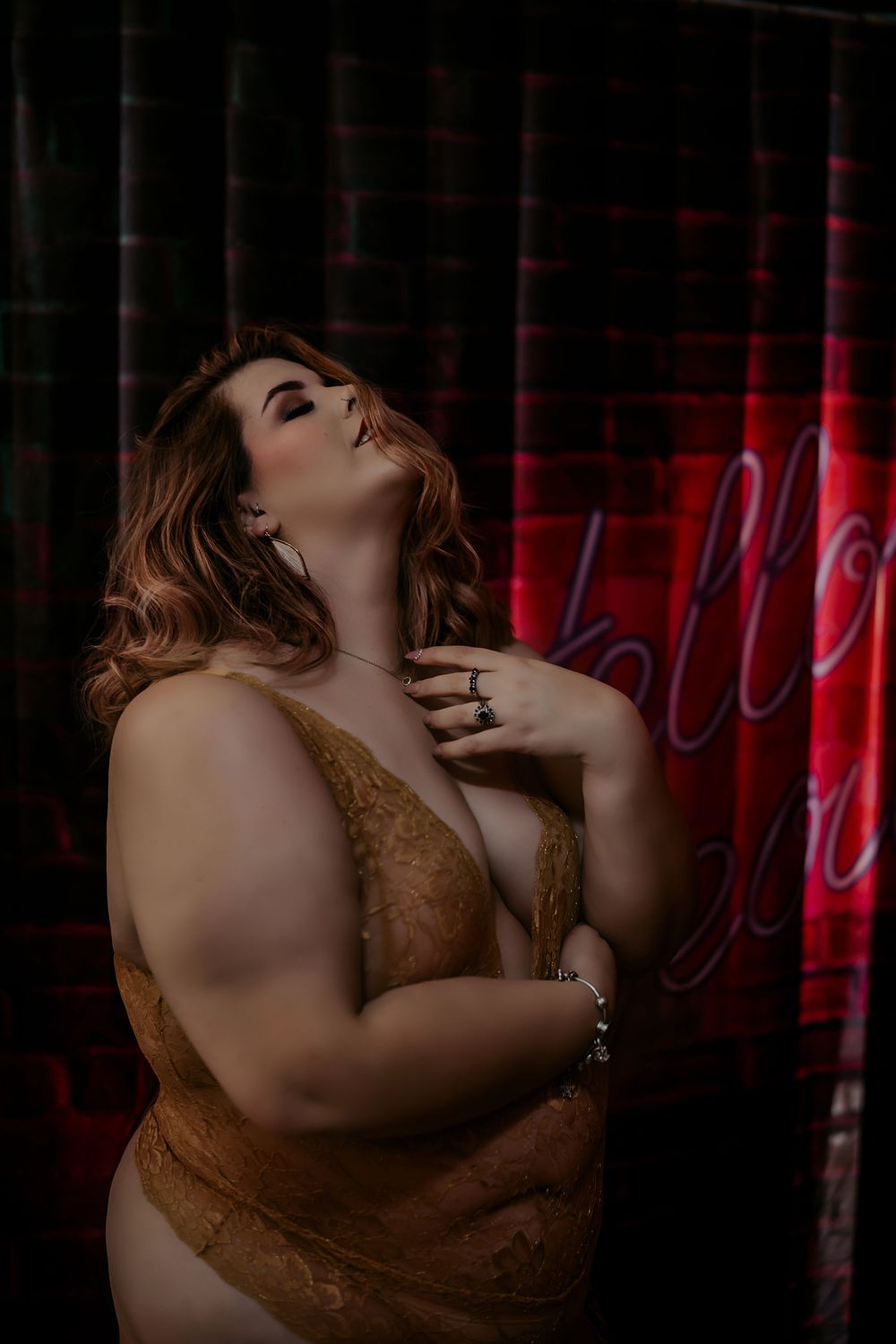 Artistic boudoir portrait featuring curvy figure in brown lace against dark background with red neon light.