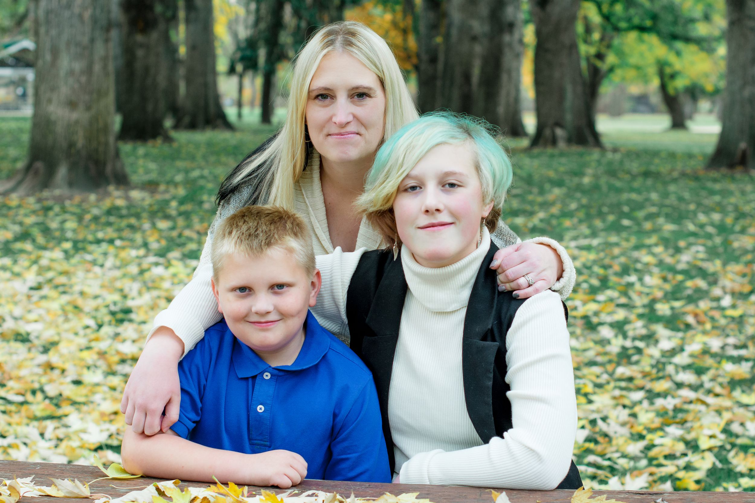 Family autumn portrait session with fallen leaves in park setting.