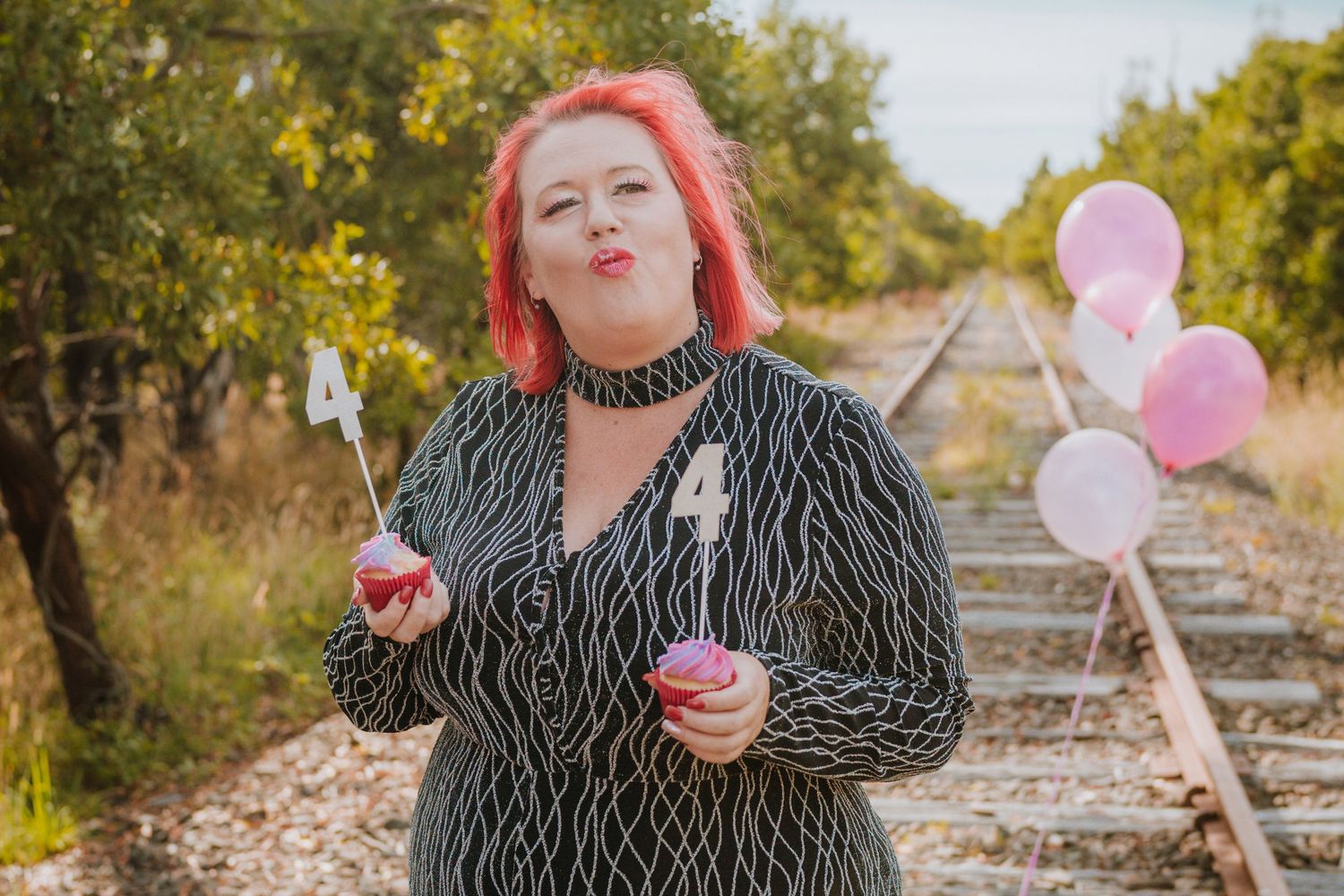 A series of playful photos taken on train tracks with pink balloons and a black and white striped jacket on a sunny day.