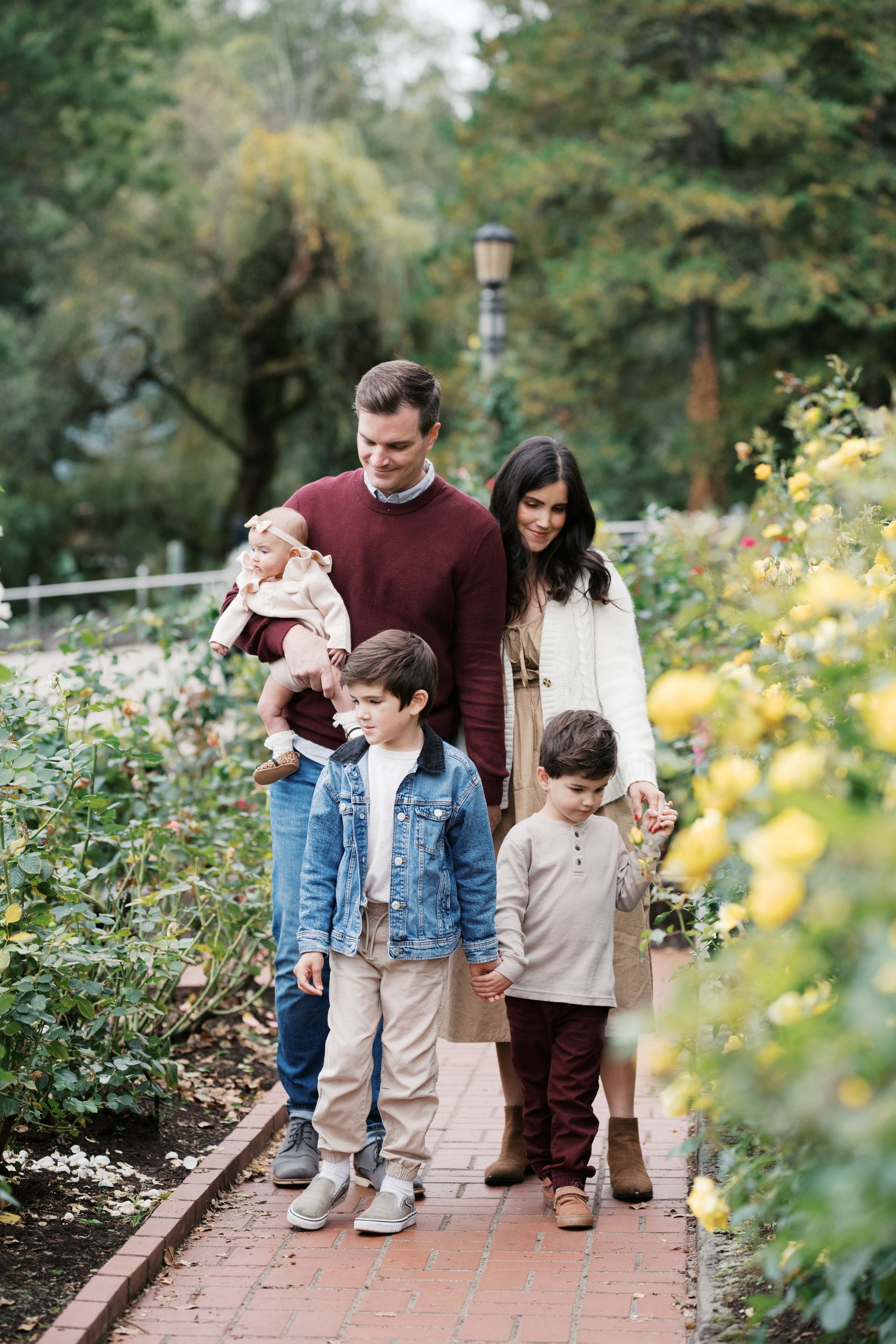 A family strolls together along a brick path in a garden with blooming yellow flowers and greenery.