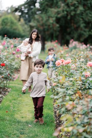 A family strolls through a garden path lined with blooming pink roses on a peaceful autumn day.