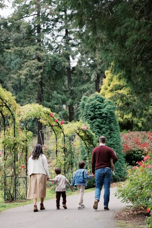 A family walks along a peaceful garden path bordered by lush greenery and arching trellises in a botanical garden.