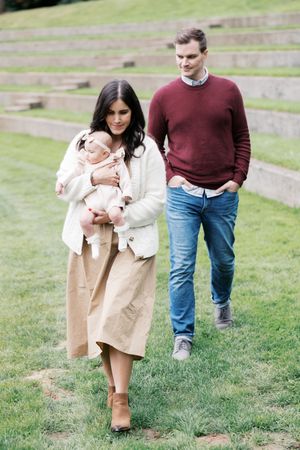 A couple stands on a grassy hill with terraced steps wearing coordinated casual fall outfits.