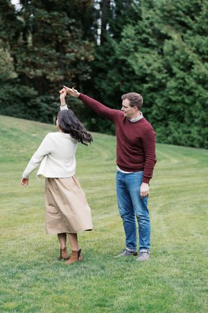 A couple dancing together on a green lawn with trees in the background.