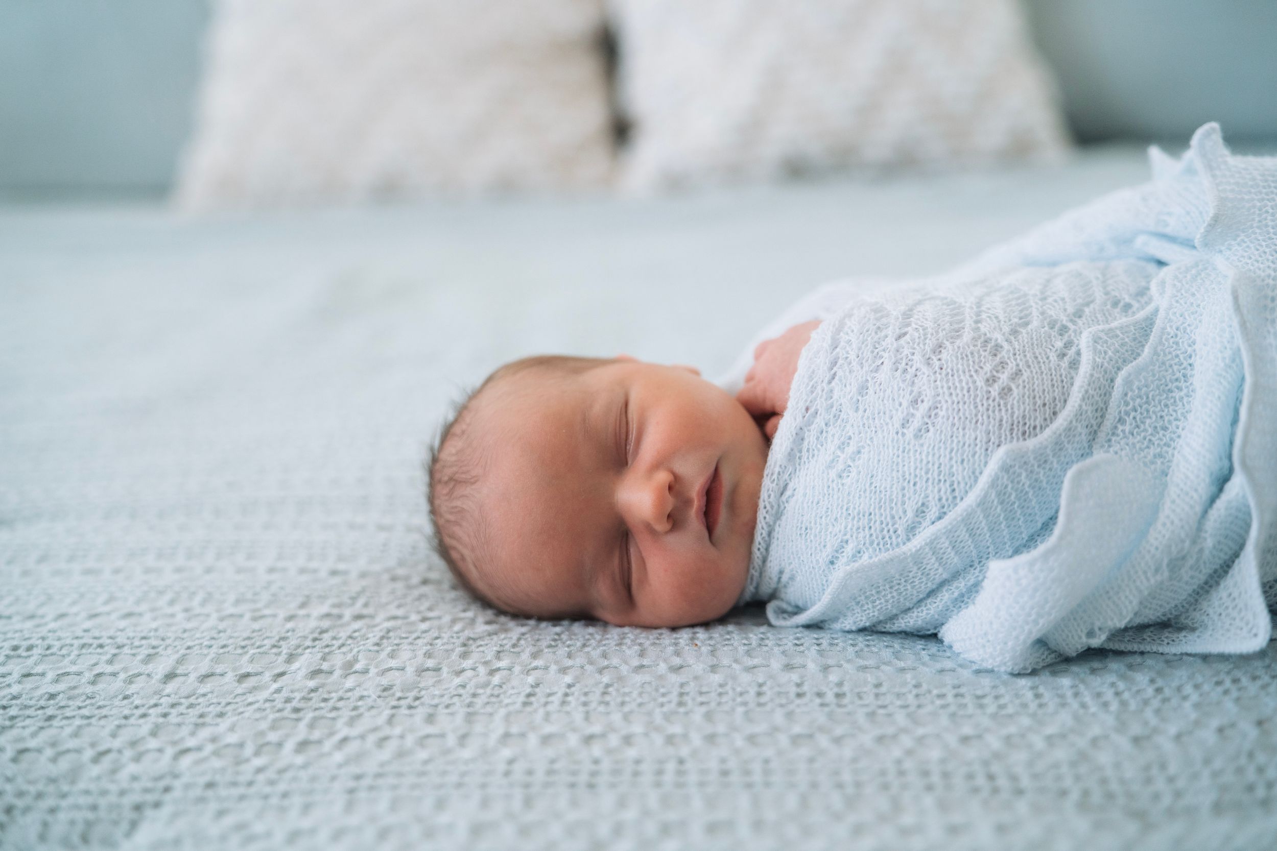A baby boy lays in a bright and airy bed for newborn pictures in the bay area