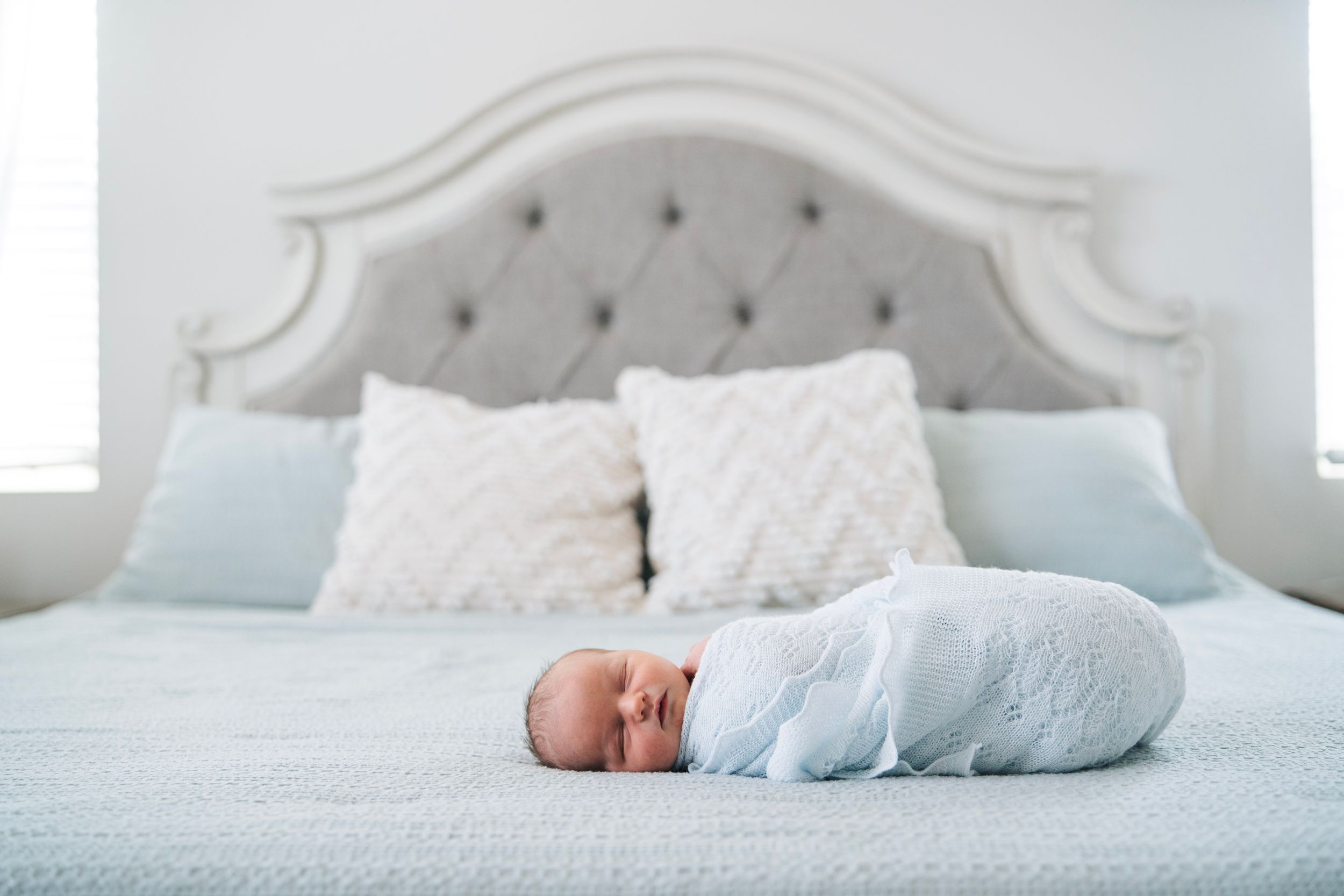 A newborn baby boy lays on a bed with a light and airy editing style