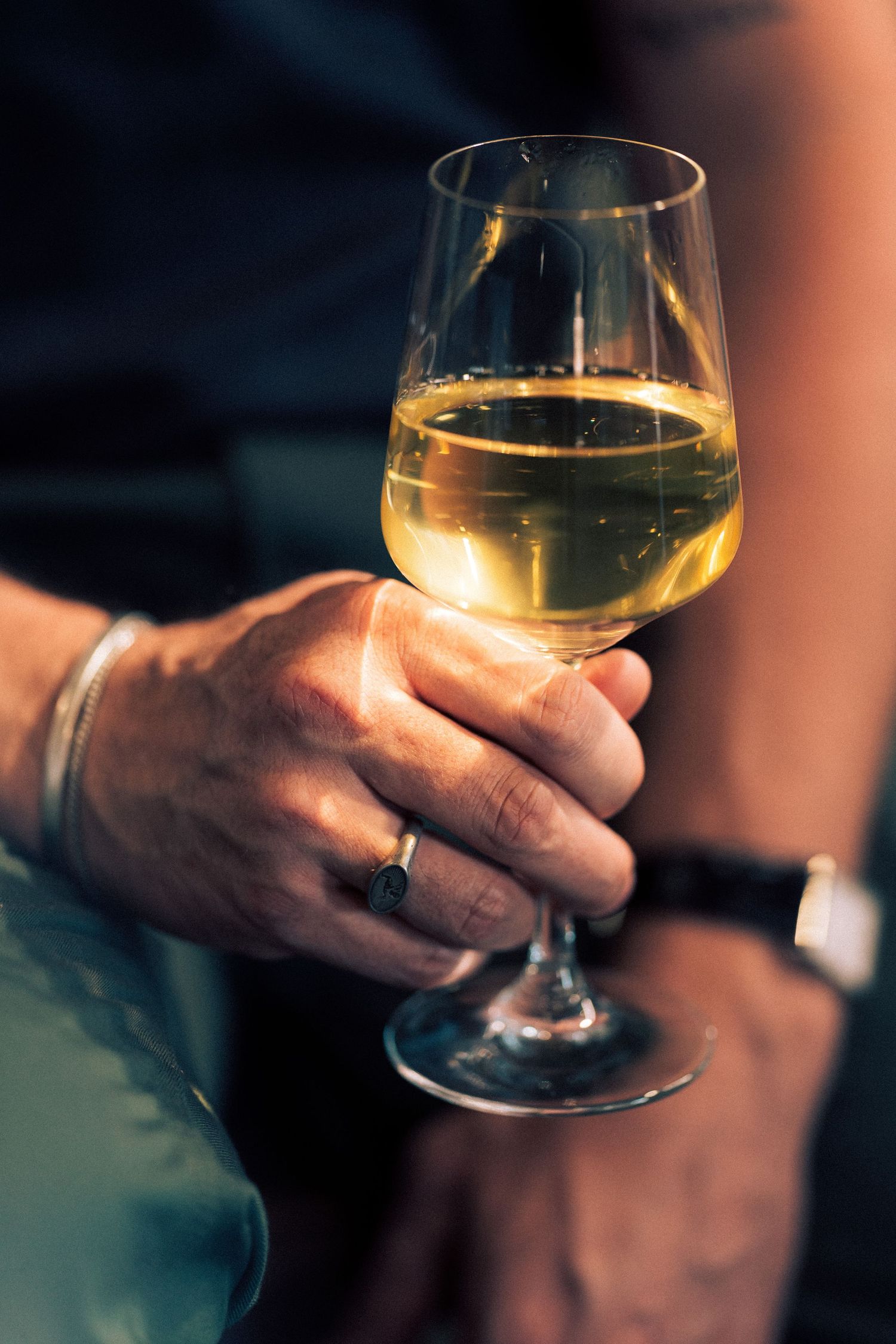 Close-up view of hands holding white wine glasses in dimly lit setting showing progression of wine tasting motion.