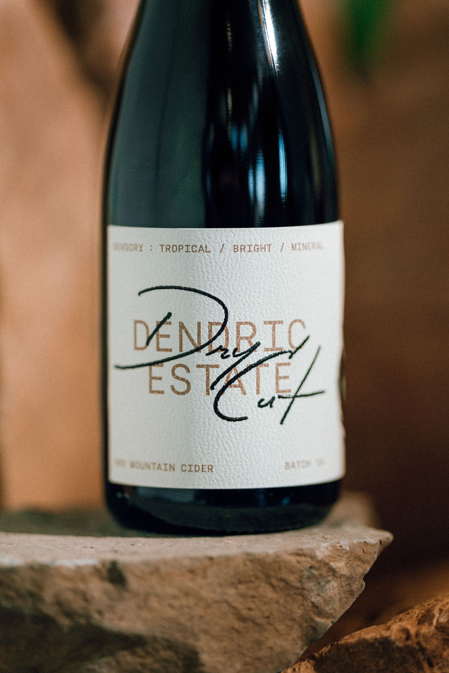 Close-up shot of a wine bottle labeled 'Denada Estate' with a signature on the label resting on a stone surface.