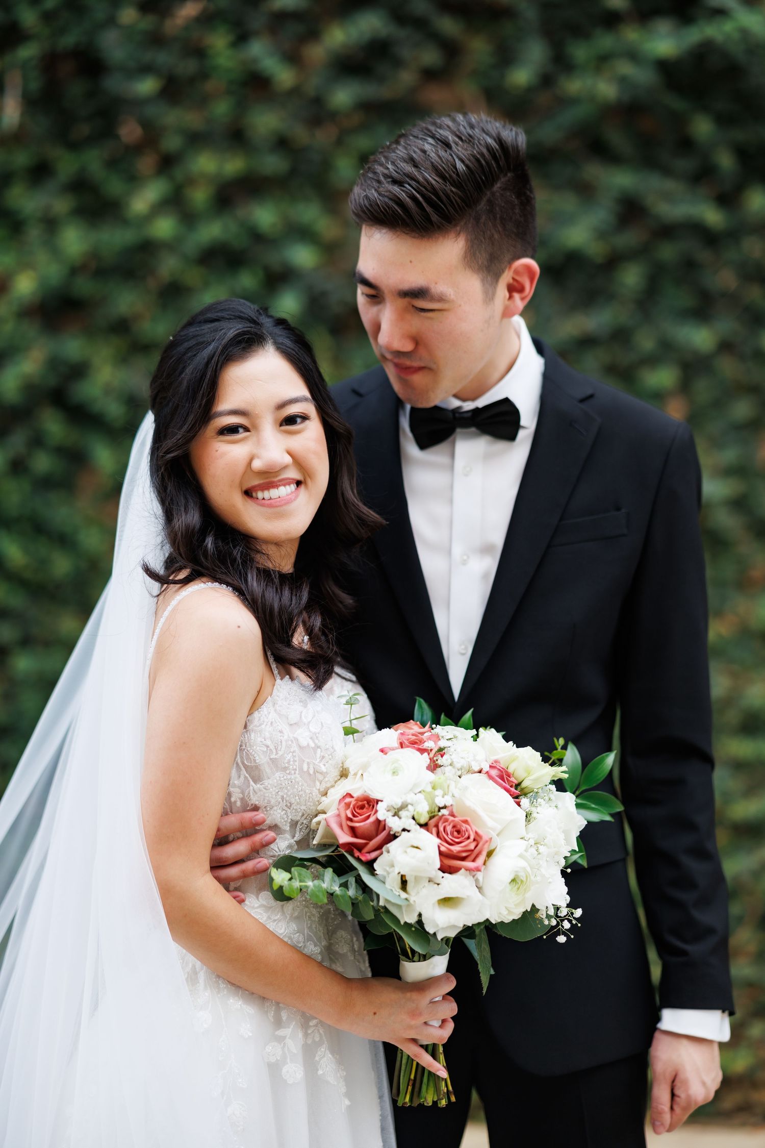 A loving couple in white and black formal attire embrace and share a happy moment together outdoors at sunset.