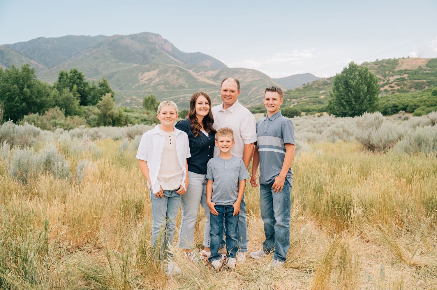 Five scenic panoramic photos show people gathered in golden grass fields with mountains in the background during sunset.