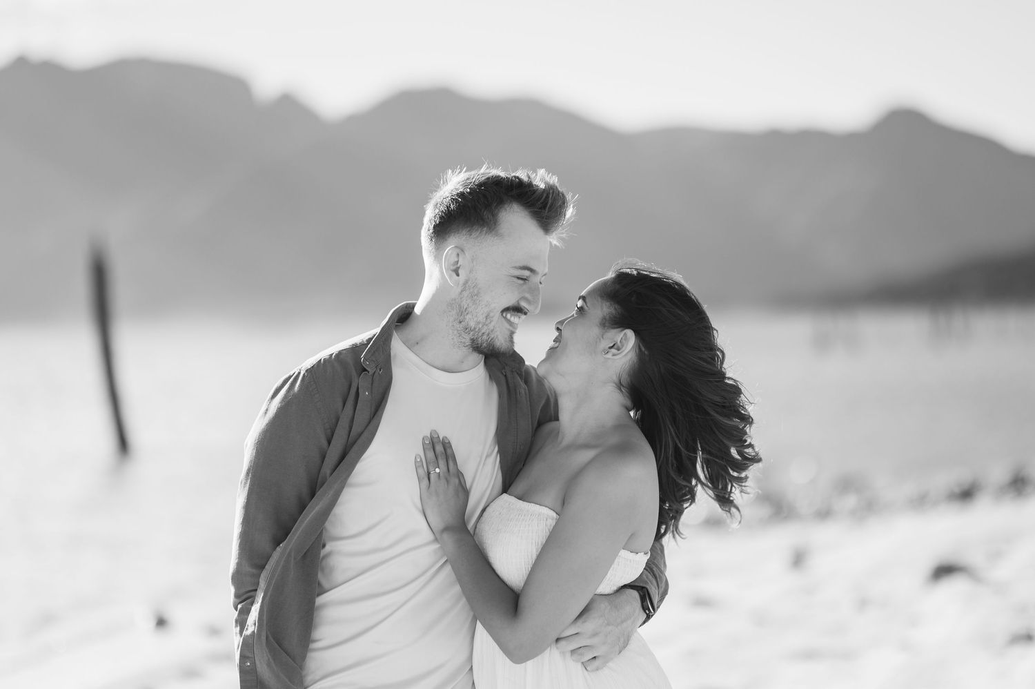 A loving couple shares a romantic kiss at sunset with mountains silhouetted in the background.