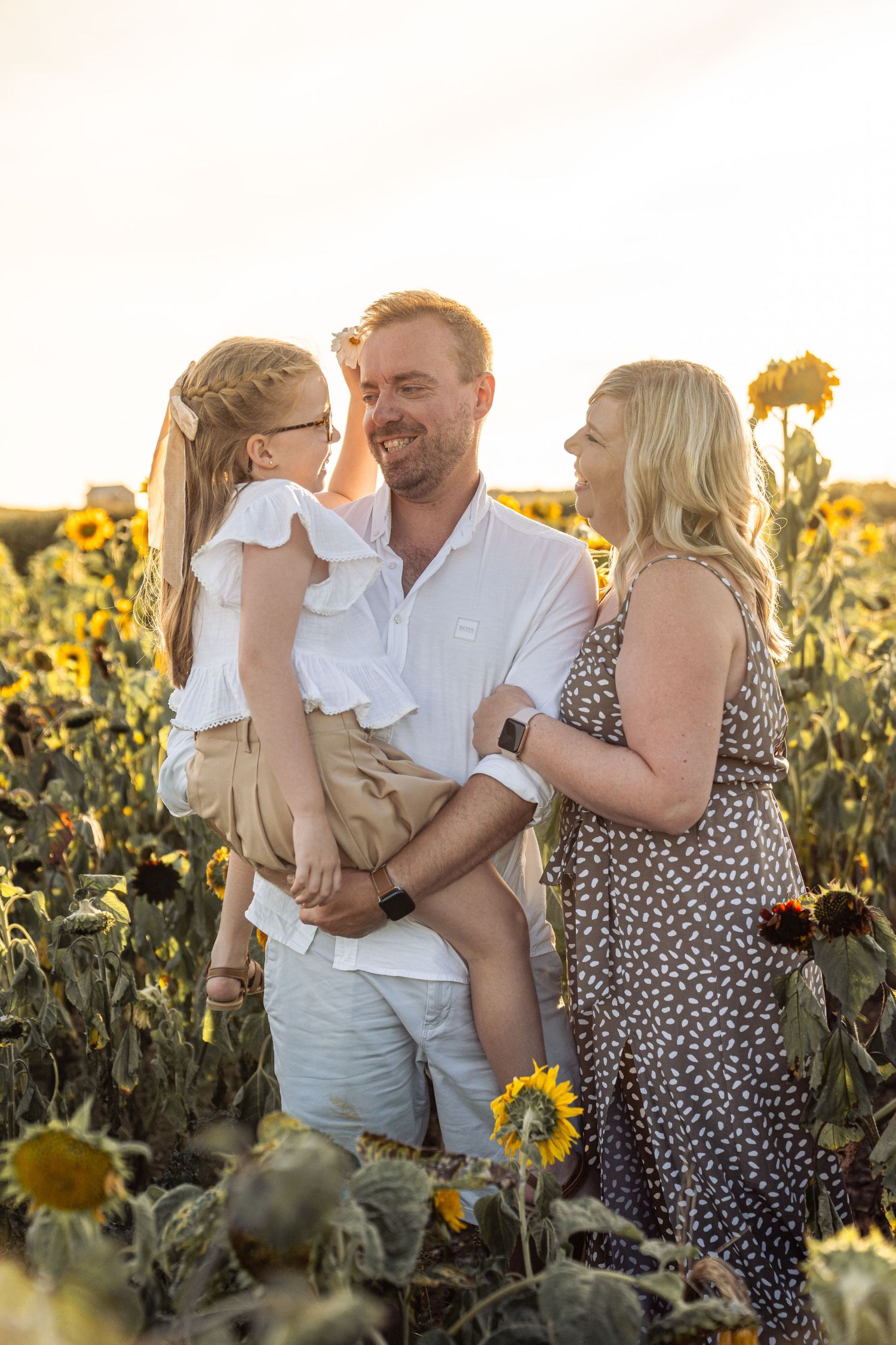 Family sharing tender moments while posing together in a sunlit sunflower field at sunset.