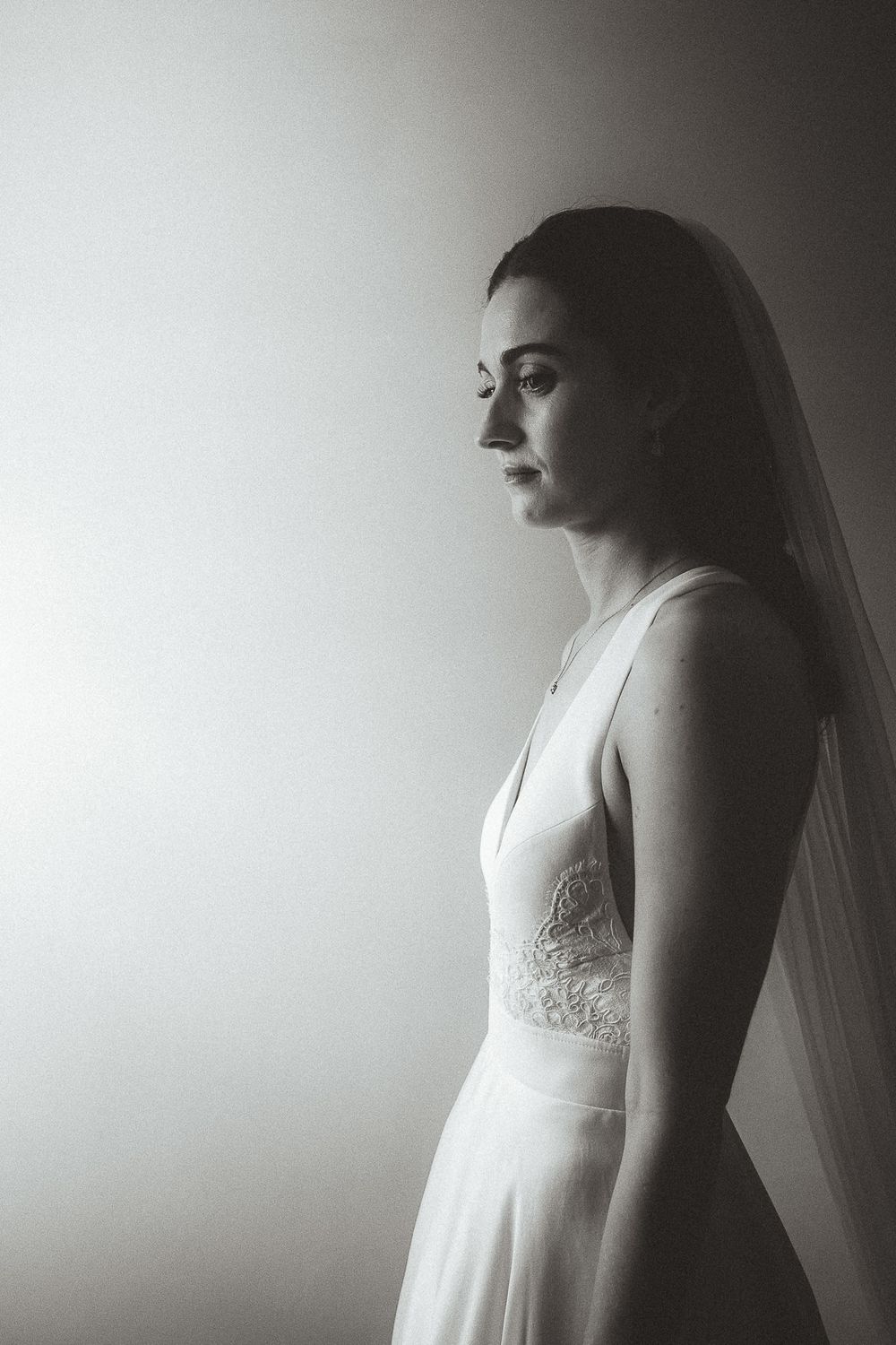 A dreamy black and white bridal portrait in profile view shows a bride wearing a delicate lace wedding gown with veil.