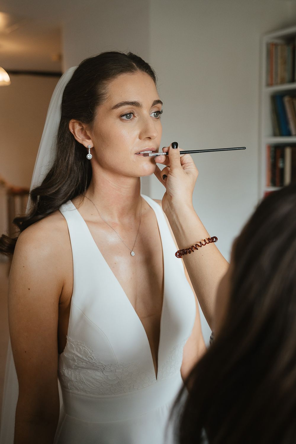 Makeup artist applies lip product on bride wearing elegant white v-neck wedding dress during preparation session.
