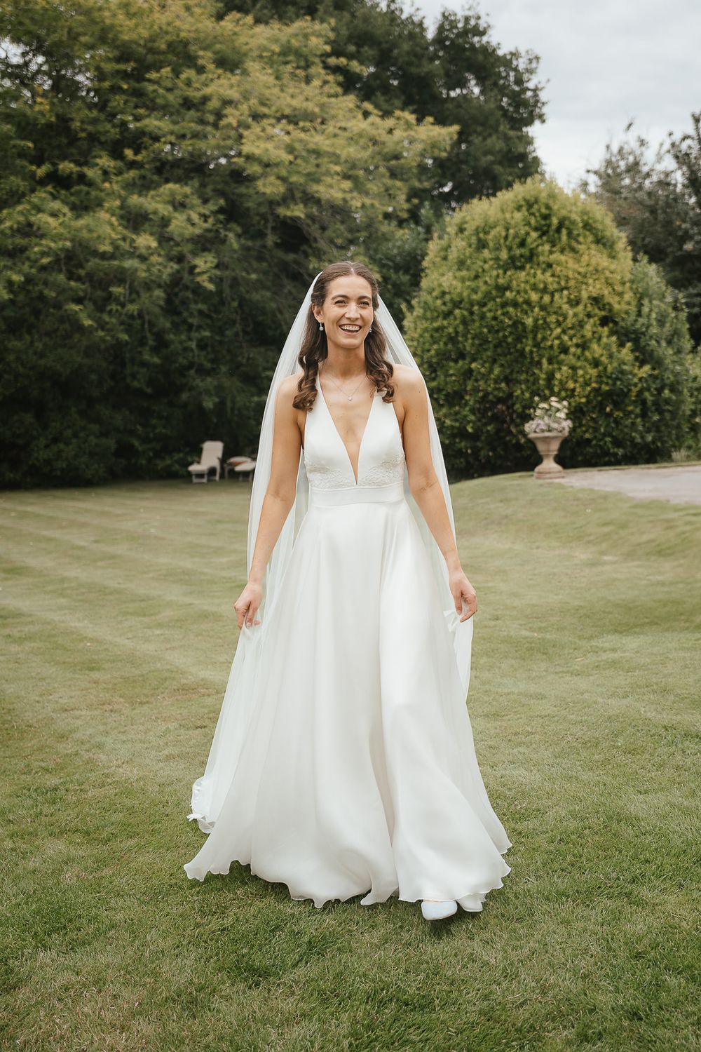 Elegant white wedding dress with plunging neckline and flowing skirt photographed in a garden setting with green foliage.