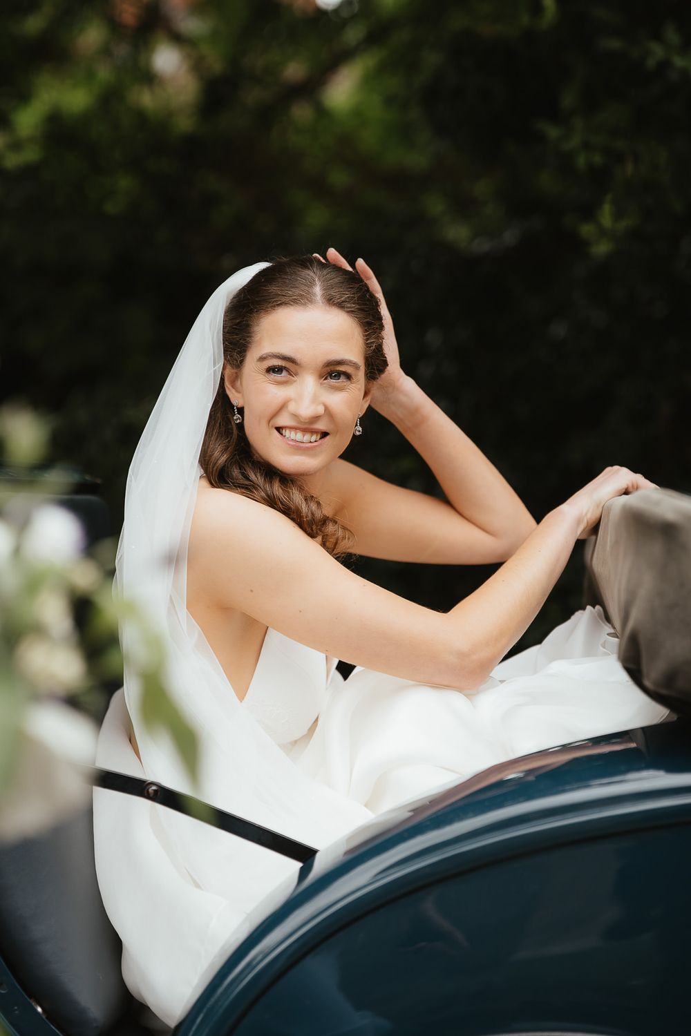 Someone in a white wedding dress smiles joyfully while sitting in a car.
