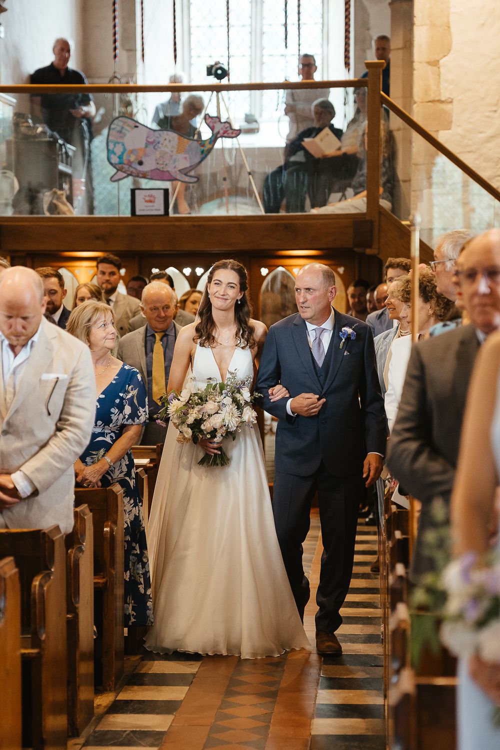 A beautiful church wedding ceremony as a bride walks down the aisle escorted in a traditional stone interior.