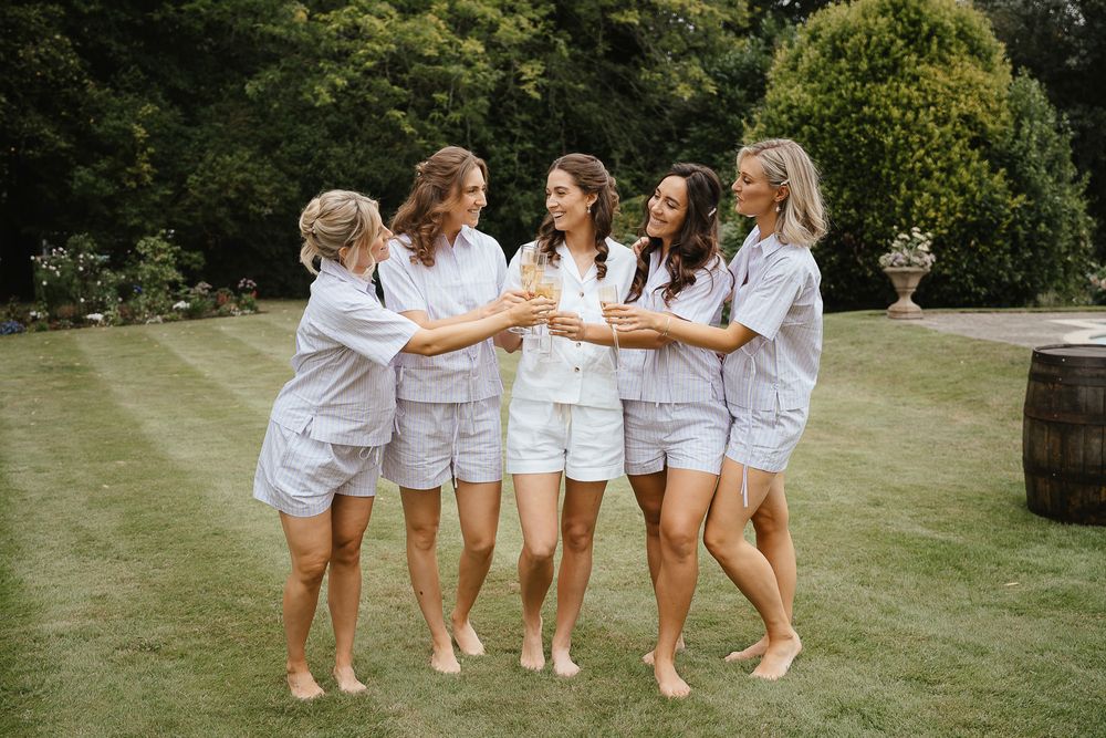 A group in matching white outfits walks arm-in-arm across a sunny lawn during an outdoor celebration.