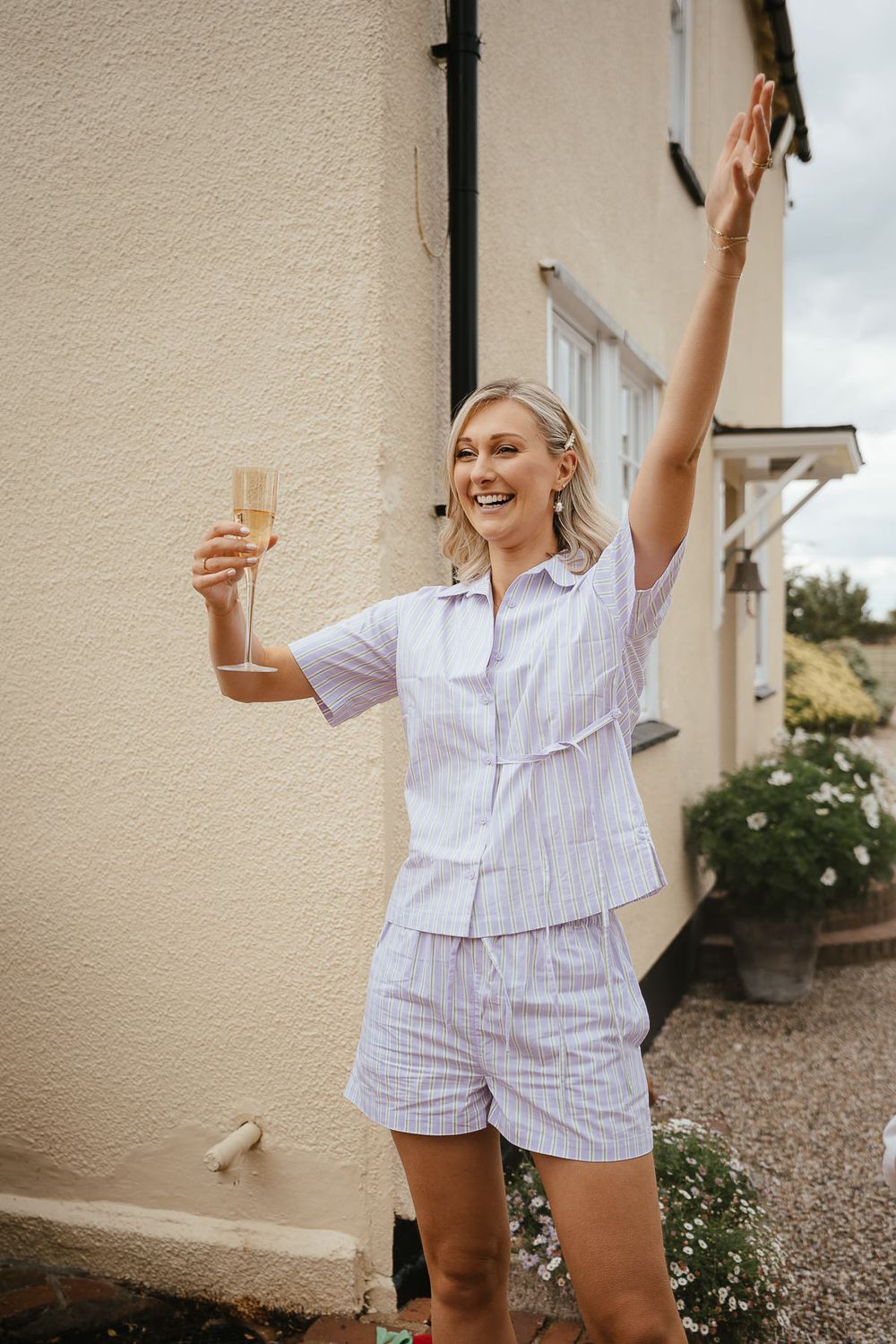 Joyful person in striped pajama set raises glass and arm in celebratory pose outside building.