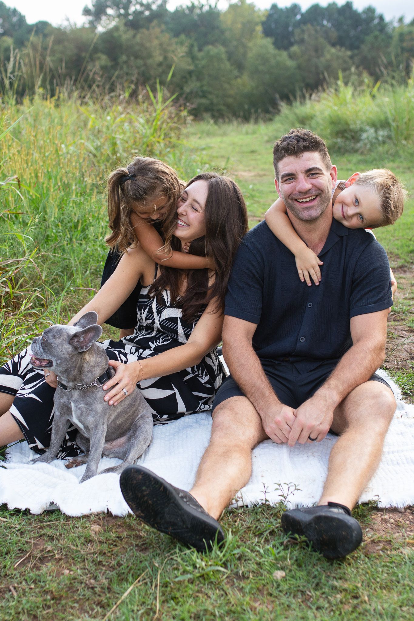 Family enjoys an outdoor picnic on a blanket with their small dog in a grassy field at NCMA