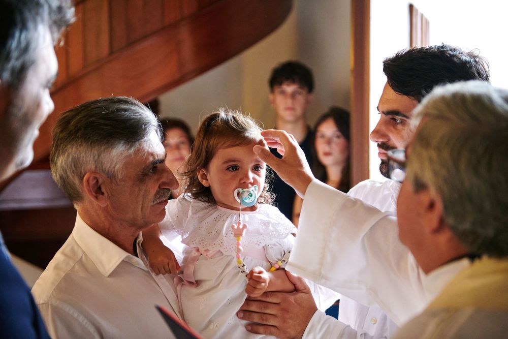 Priest performing a baptism ceremony on a young girl held by family members in a church.