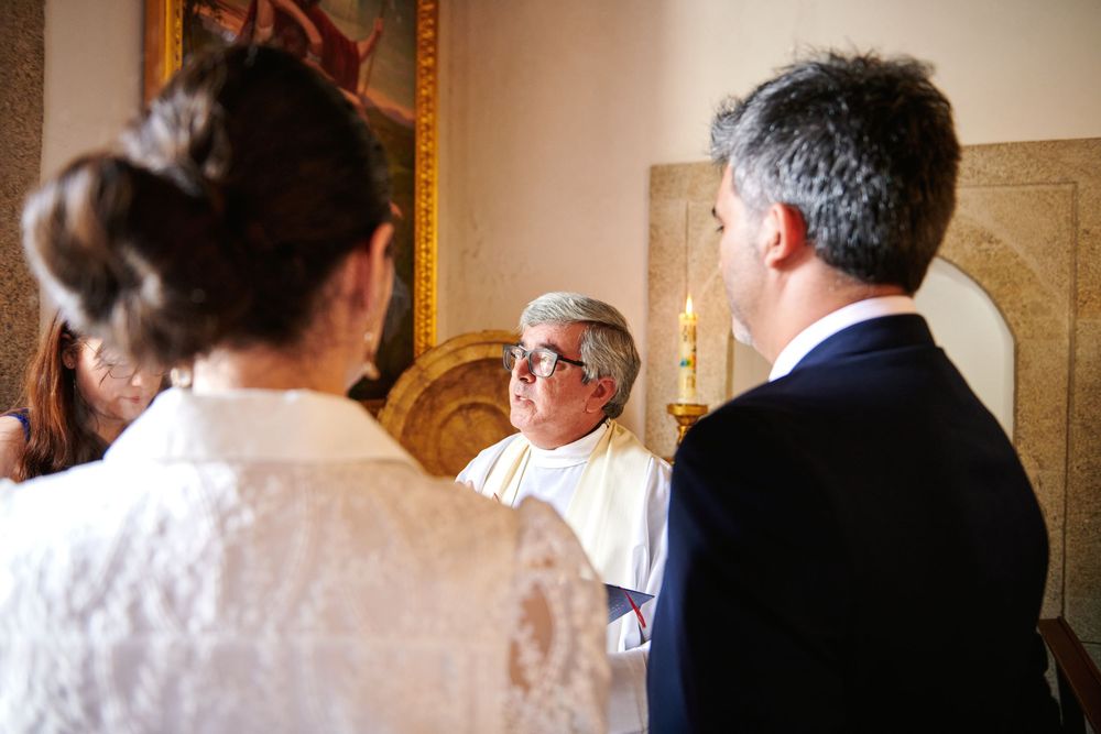 Priest officiating a religious ceremony with couple in elegant attire inside a chapel.