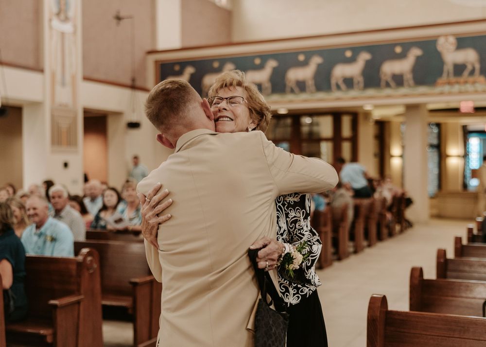 Two people sharing an emotional embrace in a church aisle surrounded by wooden pews.