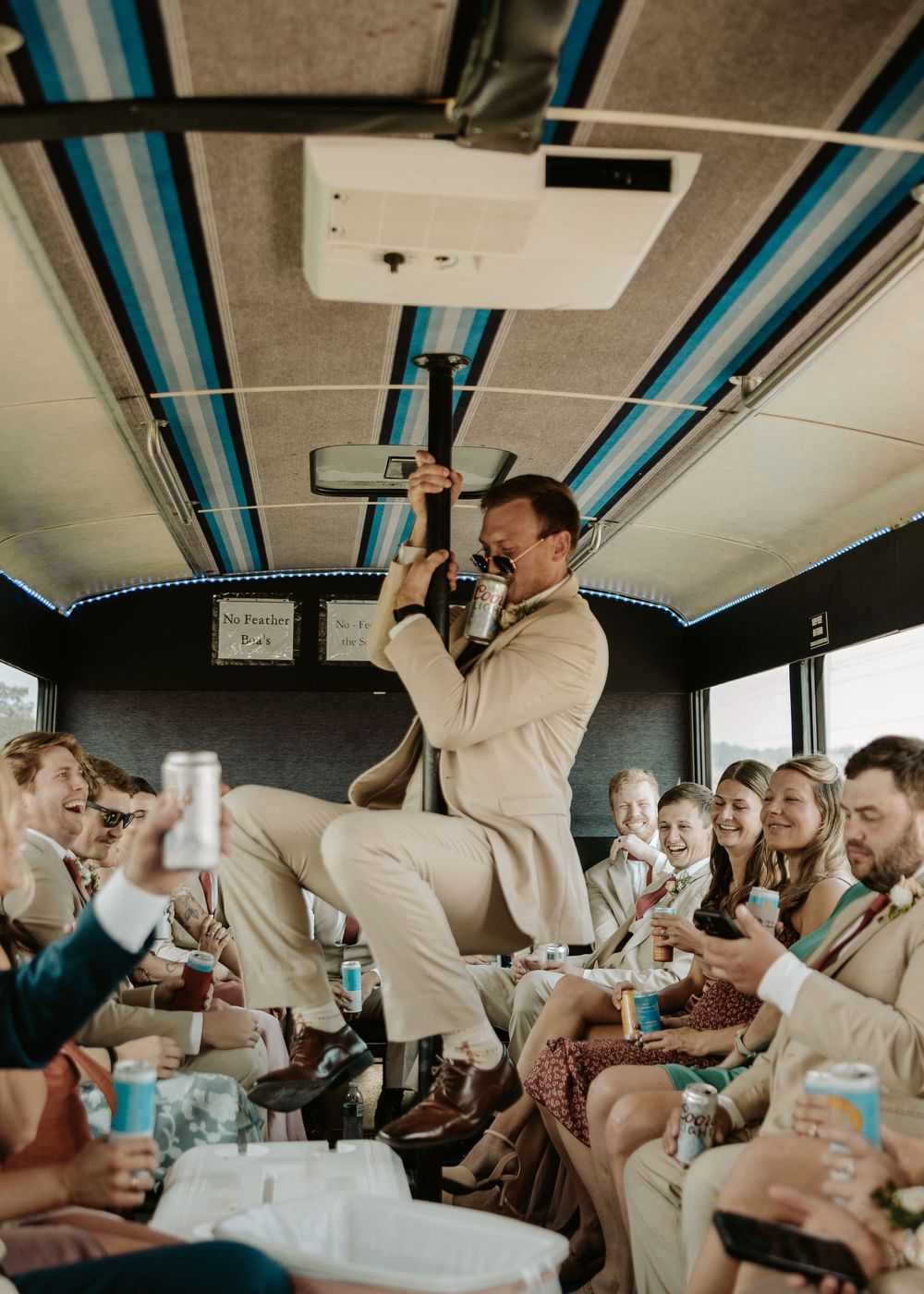 Party bus celebration with photographer standing on seat capturing energetic moments while guests enjoy drinks.