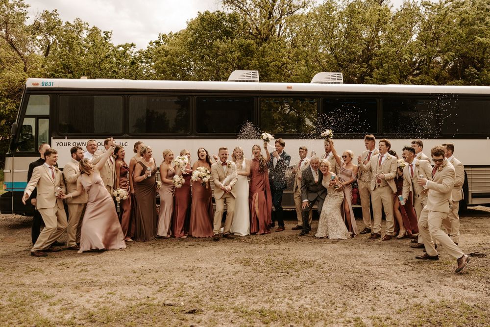 Large wedding party lined up outdoors for a group photo in neutral tones.
