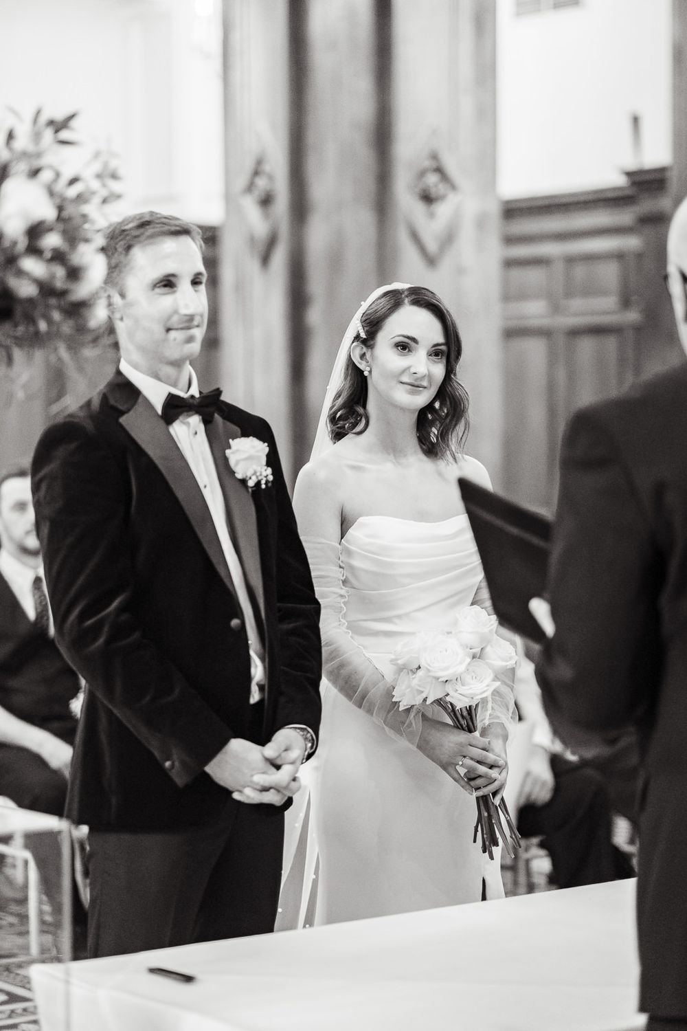 A couple in formal wedding attire stands at the altar during their ceremony in a black and white photo at intimate london wedding.