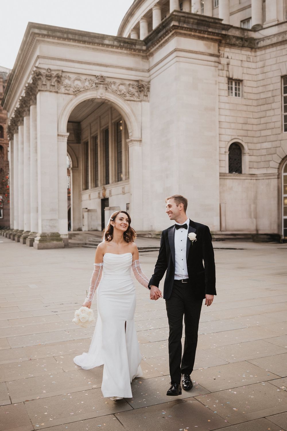 Bride and groom share playful moments in front of a grand classical stone building during their intimate london wedding.