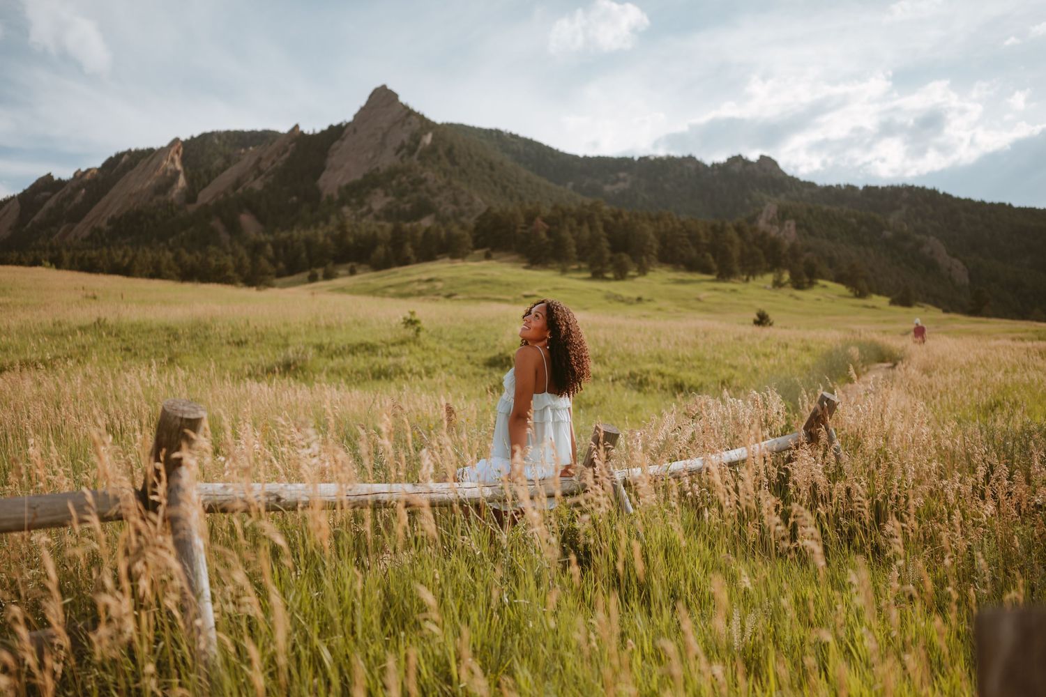 A scenic mountain meadow in Colorado with tall grass and rustic wooden fence posts beneath the Flatirons peaks.