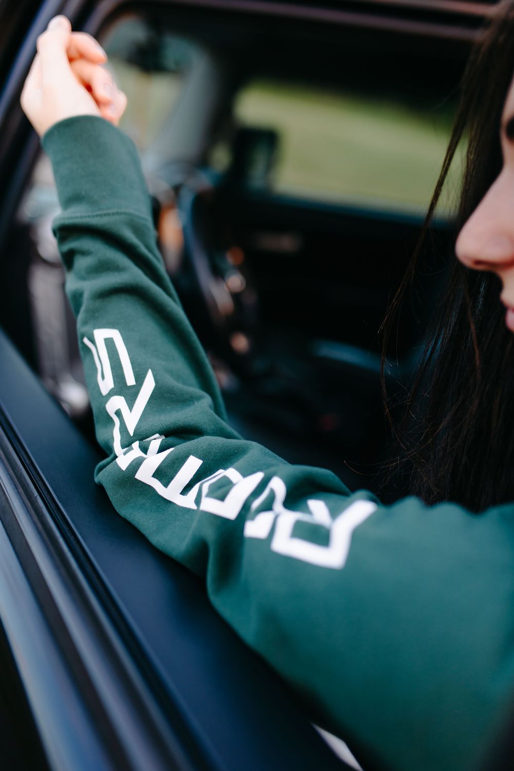 Close-up of a green sweater with white text design worn while driving a car.