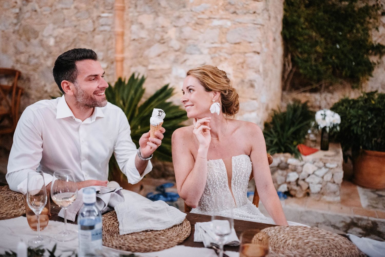 Braut und Bräutigam lachen vertraut während er ihr sein Eis anbietet bei ihrer mallorquinischen Hochzeitsfeier im Freien an der Finca.