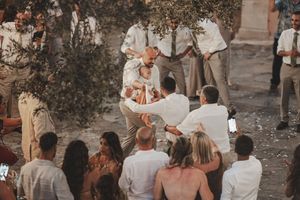 Wedding guests dance and socialize at an outdoor reception under string lights at dusk.