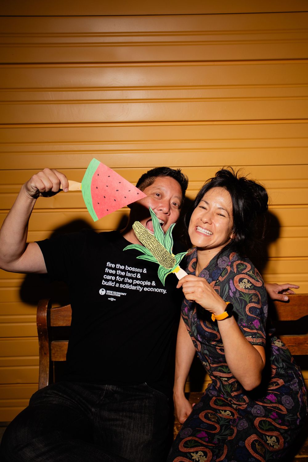 Playful moment with watermelon-shaped props against wooden wall background.