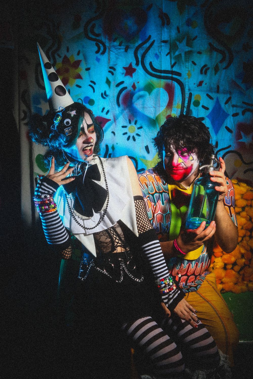 A dramatic sequence of clown performers in striped clothing against a vibrant graffiti wall with blue and yellow colors.