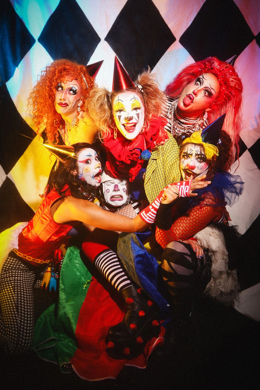Performers in colorful costumes and dramatic makeup pose playfully in a series of theatrical shots with geometric backgrounds.