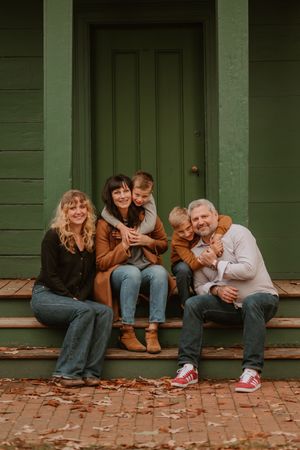 A family sits together on green wooden porch steps during autumn.